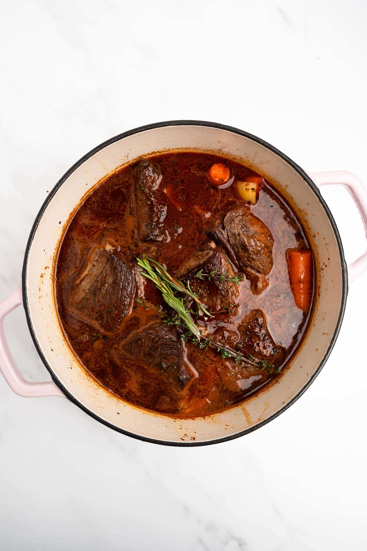 short ribs in a pot with beef broth topped with herbs.