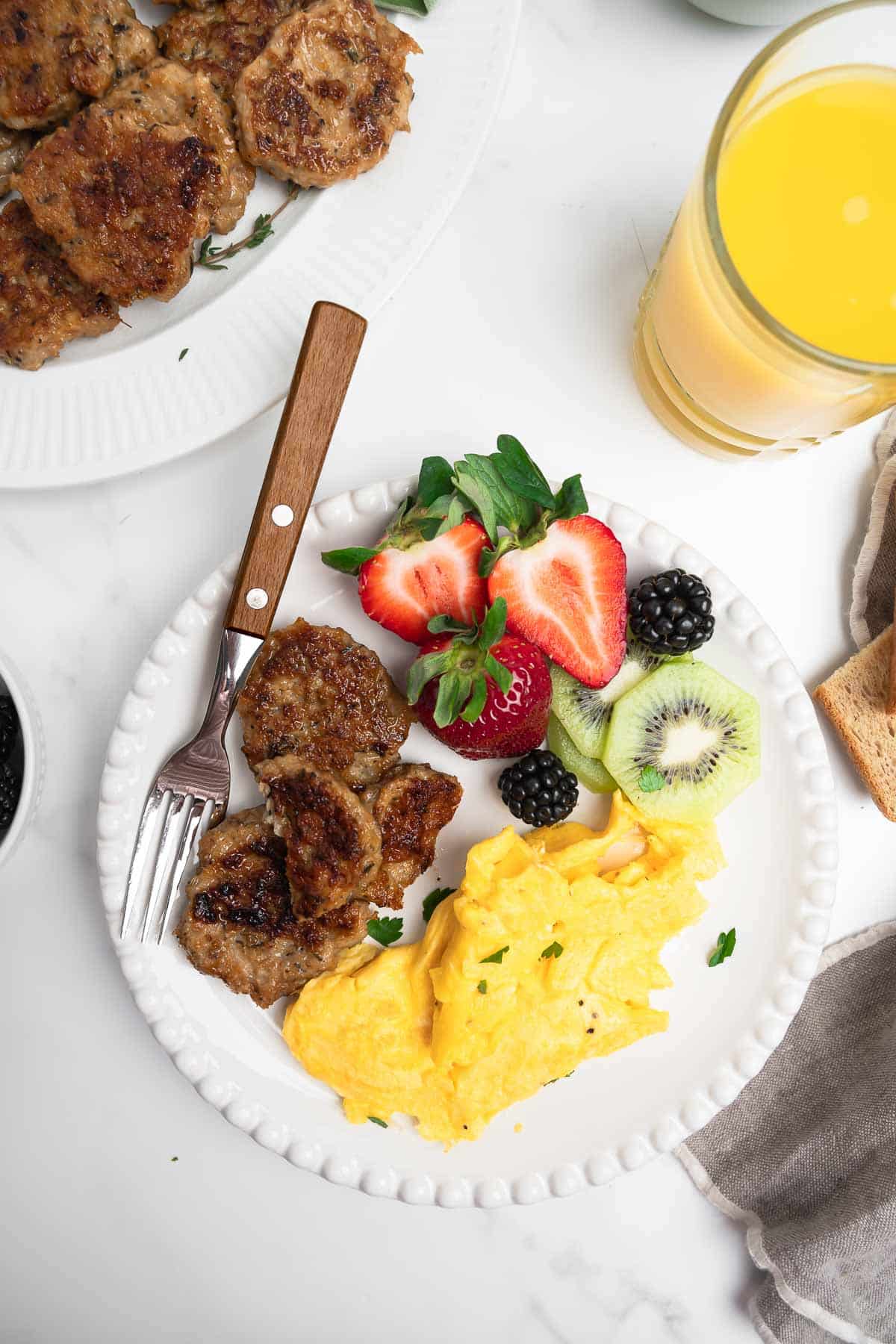chicken sausage, fruit and eggs on a white plate with a fork.