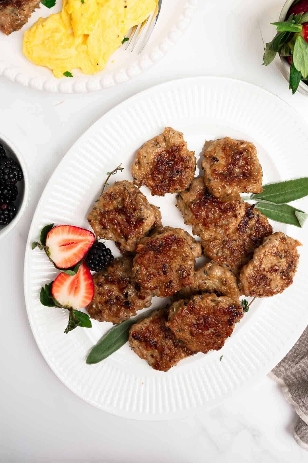 maple chicken sausage patties on a white platter with fruit and sage.