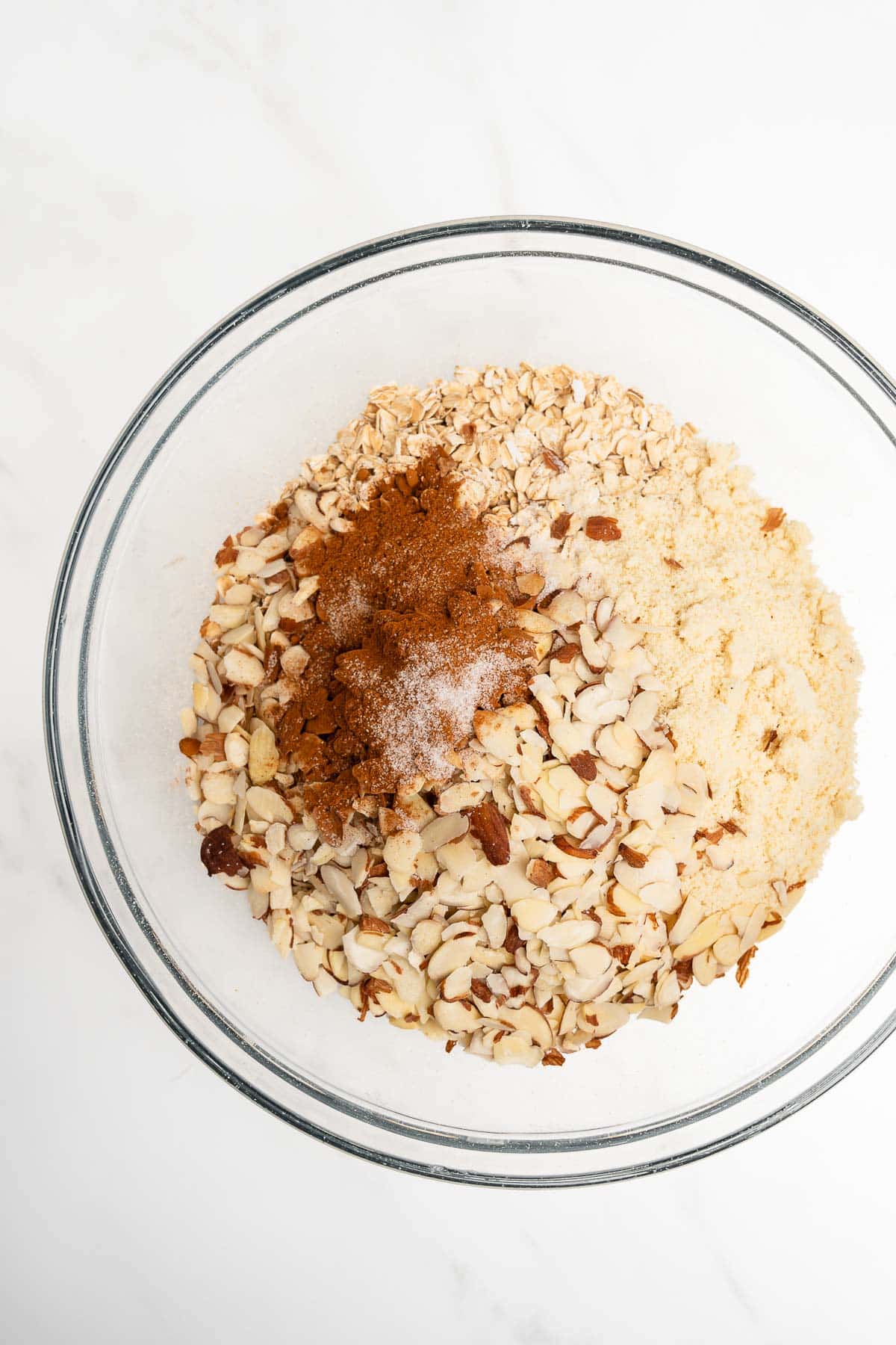 top view of oats, almonds, almond flour, and cinnamon in a glass mixing bowl.