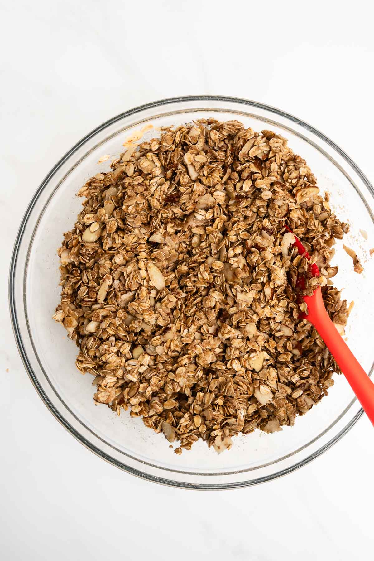 over head view of oats coated in coconut oil mixture in glass bowl.