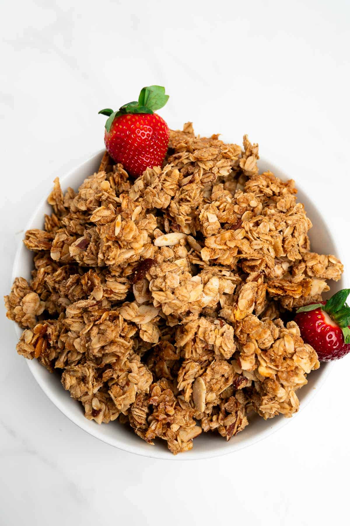 homemade granola clusters in a bowl with two strawberries.