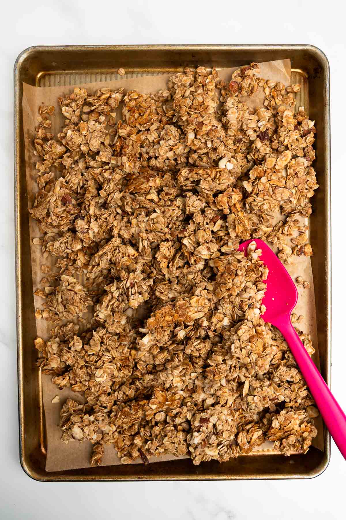 granola on a baking sheet with pink spatula.
