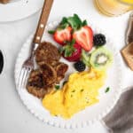 chicken sausage, fresh fruit and scrambled eggs on a white plate with a fork.