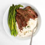 slices of reverse sear steak on a plate with mashed potatoes and asparagus.