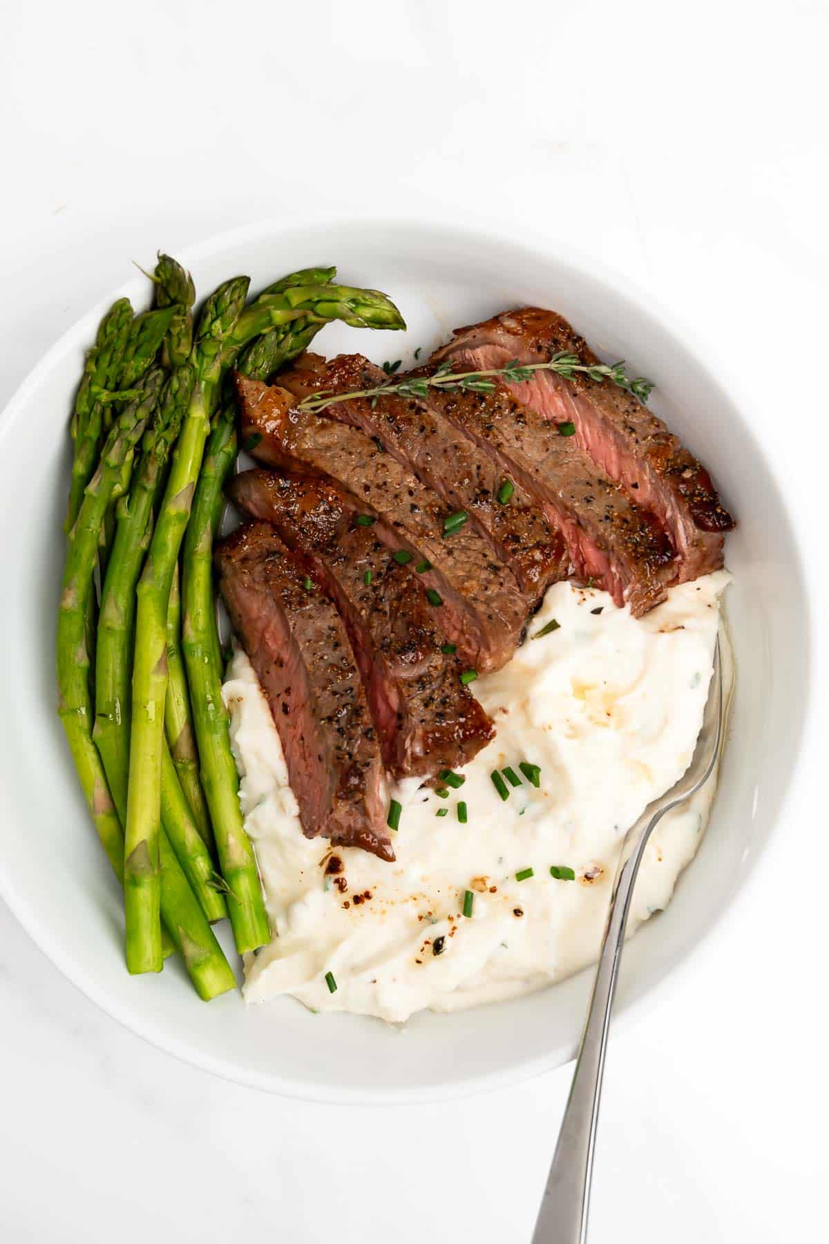 slices of reverse sear steak cooked medium with mashed potatoes and asparagus.