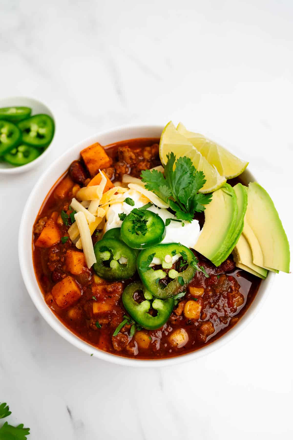 sweet potato turkey chili in a bowl topped with shredded cheese and avocado.