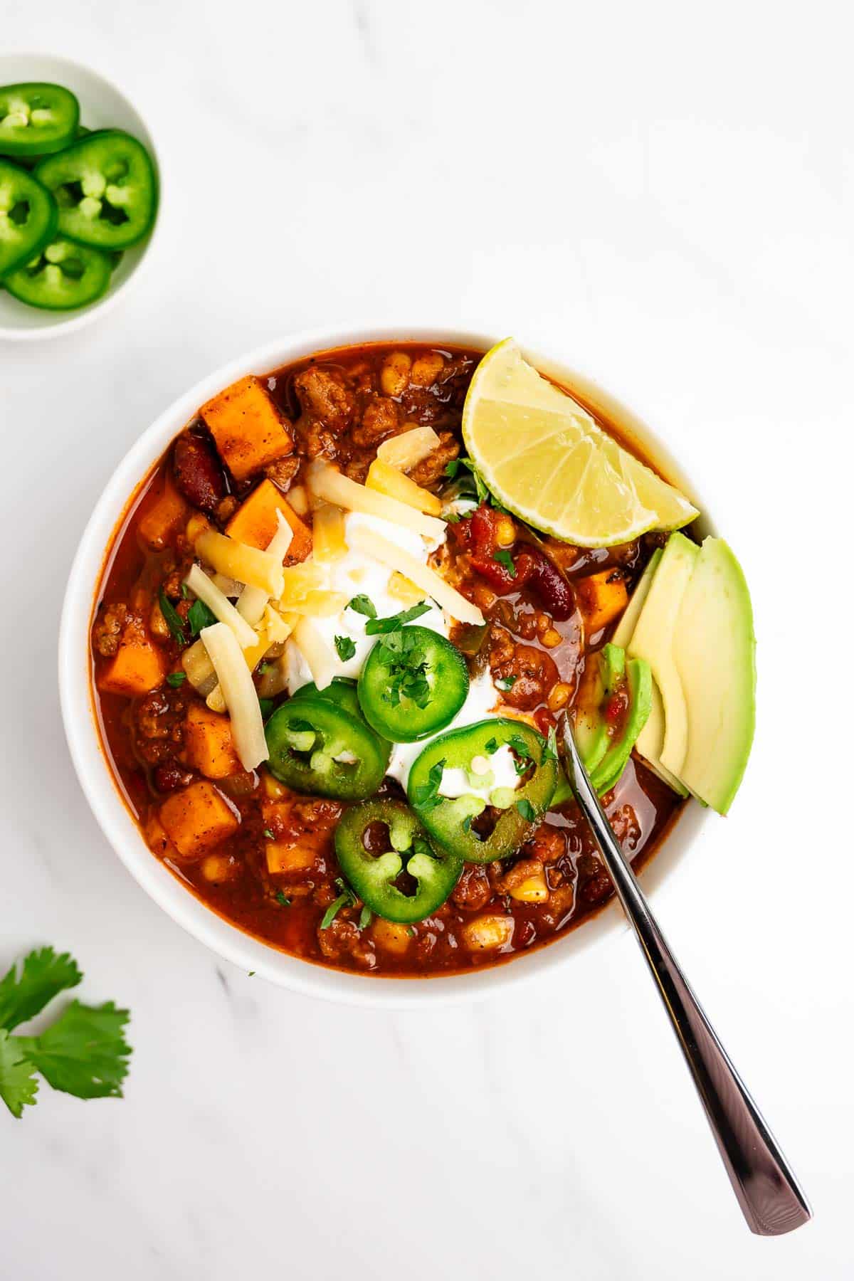 turkey sweet potato chili in a bowl with spoon topped with shredded cheese.