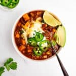 turkey sweet potato chili in a bowl with spoon topped with cheese and sour cream.