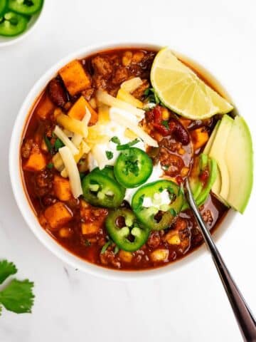 turkey sweet potato chili in a bowl with spoon topped with cheese and sour cream.