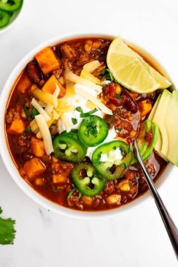 turkey sweet potato chili in a bowl with spoon topped with cheese and sour cream.
