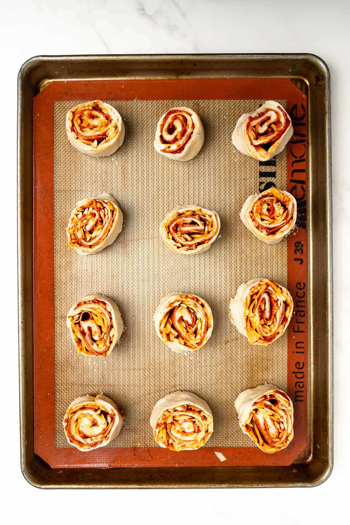 twelve unbaked pizza rolls on a baking sheet.