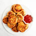 pepperoni pizza rolls stacked on a plate with a small bowl of pizza sauce.