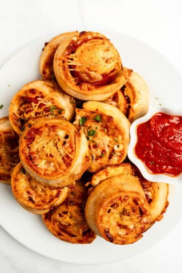 pepperoni pizza rolls stacked on a plate with a small bowl of pizza sauce.