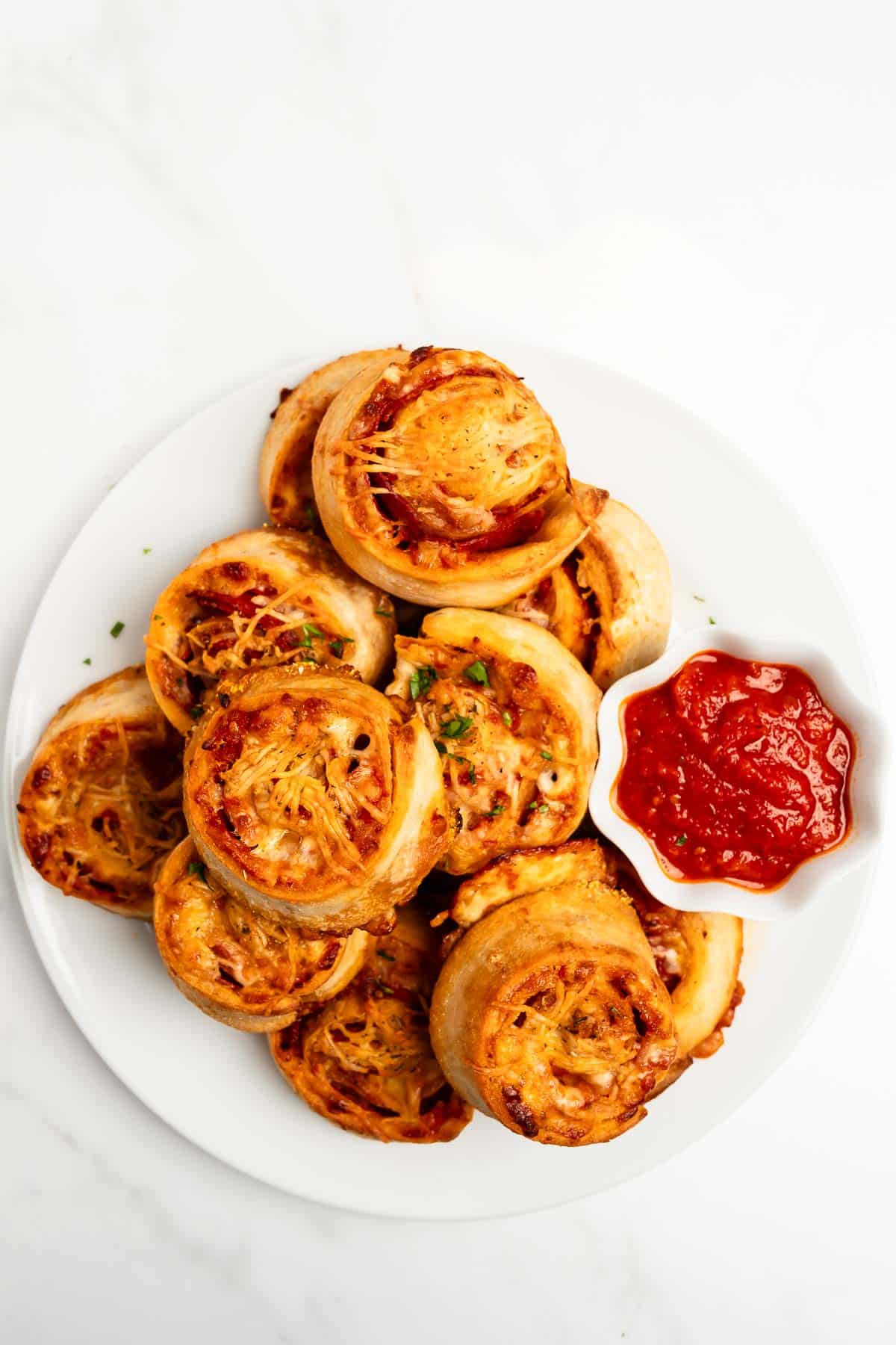 pepperoni pizza rolls stacked on a plate with marinara sauce.