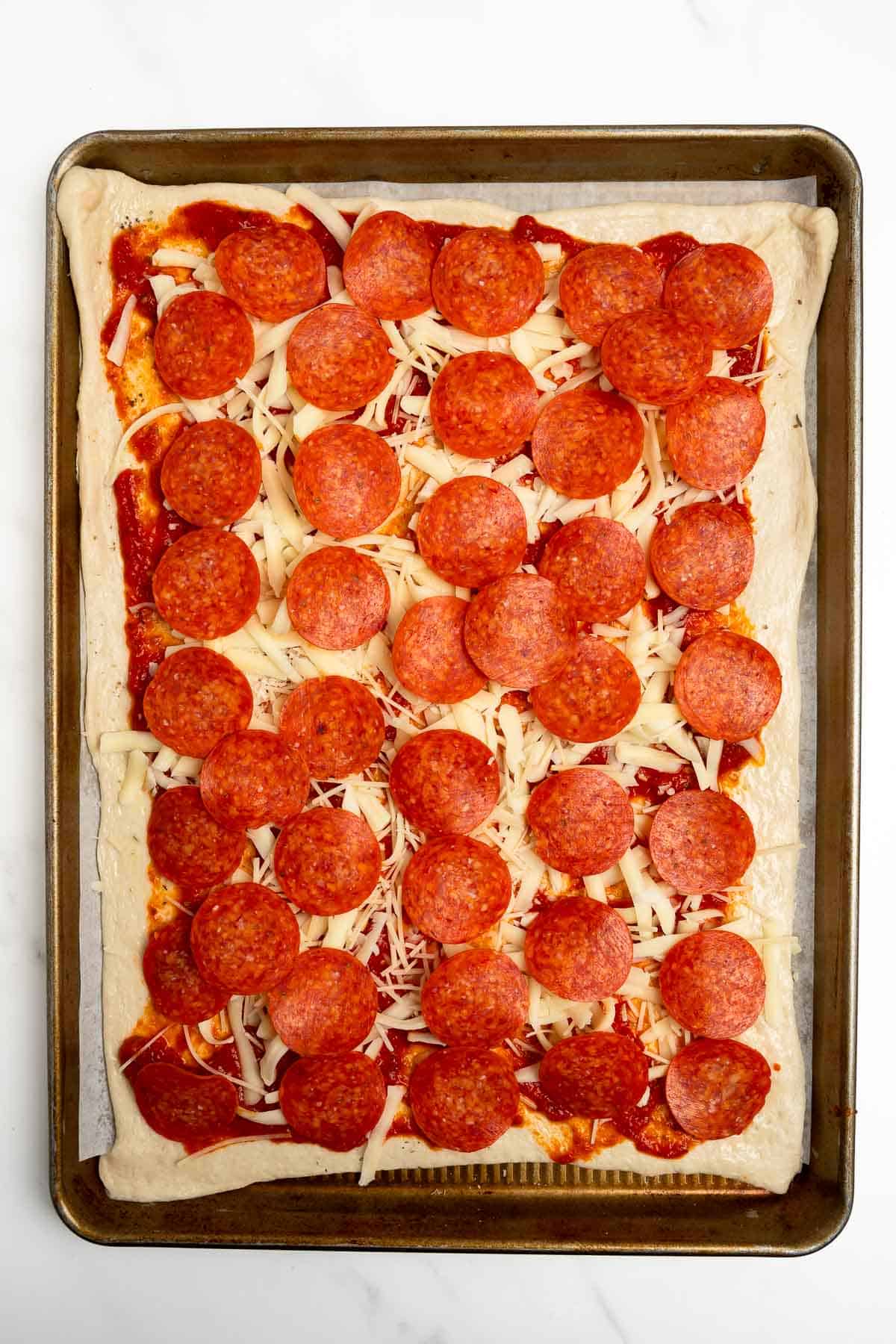 pizza dough topped with sauce, cheese, and pepperoni on a baking sheet.