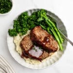 plate of sliced meatloaf over mashed potatoes with broccolini