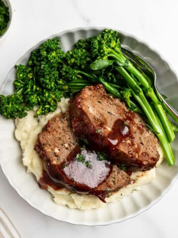 plate of sliced meatloaf over mashed potatoes with broccolini