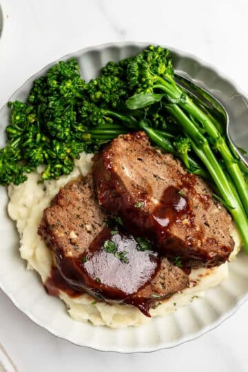 plate of sliced meatloaf over mashed potatoes with broccolini