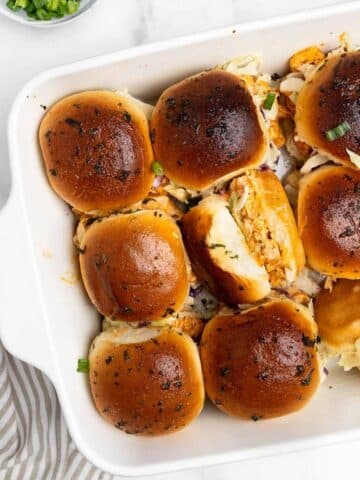 9 buffalo chicken sliders in a baking dish with one turned on the side.