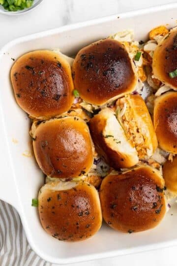 9 buffalo chicken sliders in a baking dish with one turned on the side.