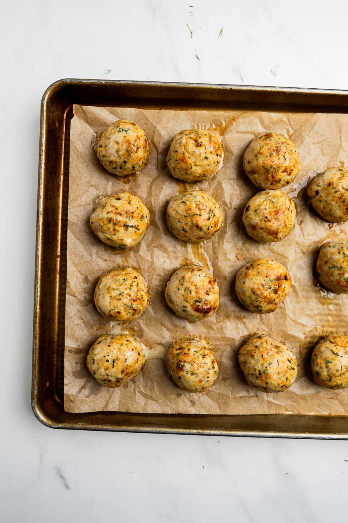 Cooked Greek chicken meatballs on a baking sheet lined with parchment paper.