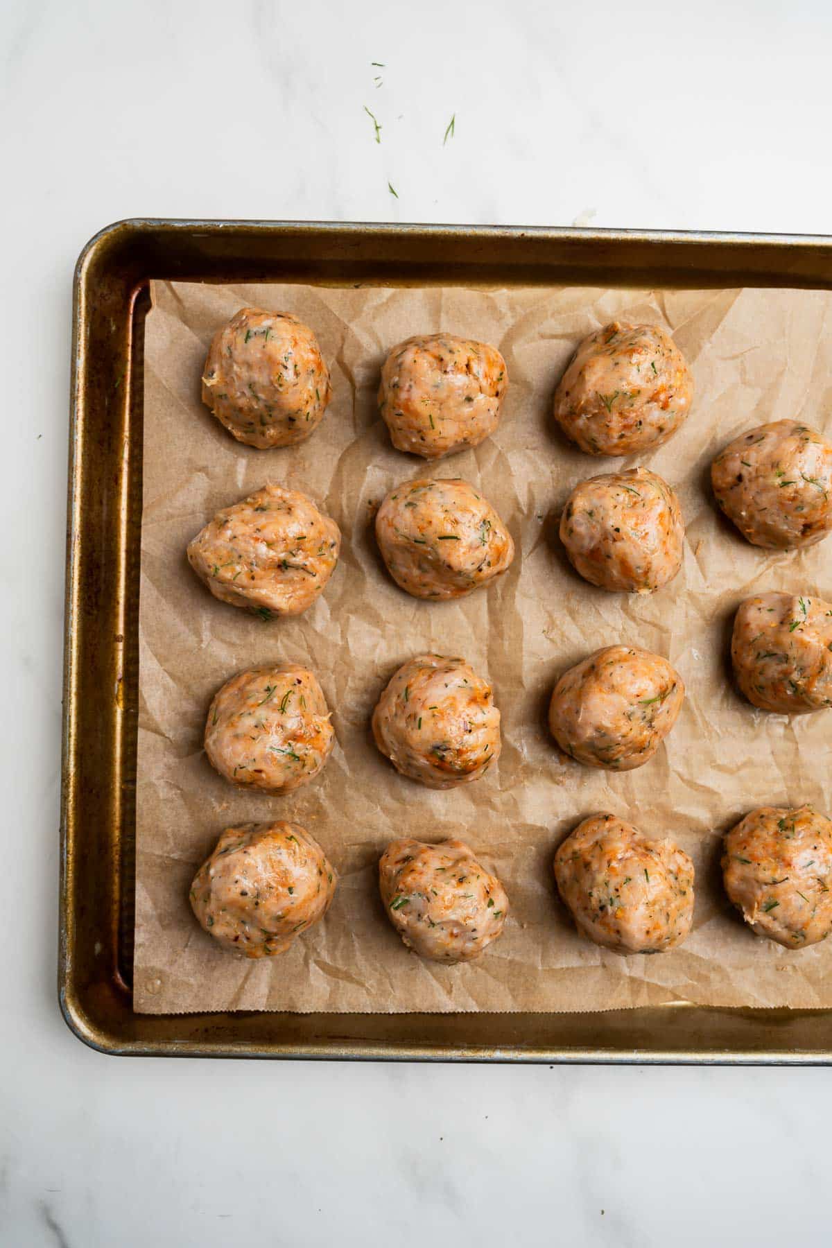Raw Greek chicken meatballs on a baking sheet lined with parchment paper.