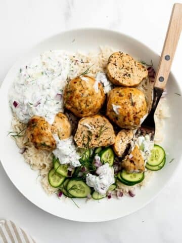 Greek chicken meatballs in a bowl with rice and cucumber.