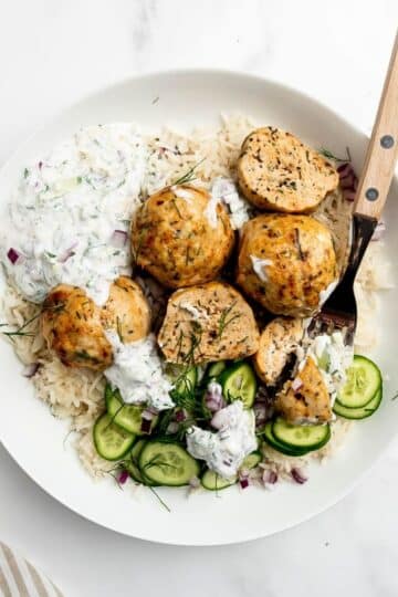 Greek chicken meatballs in a bowl with rice and cucumber.