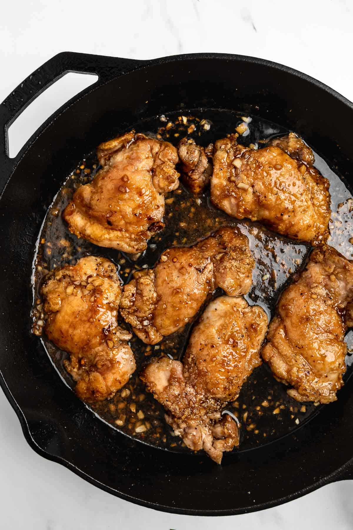 chicken thighs coated in honey garlic sauce in a cast iron skillet.