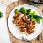 sliced honey garlic chicken over rice with broccoli on a white plate.