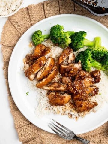 sliced honey garlic chicken over rice with broccoli on a white plate.
