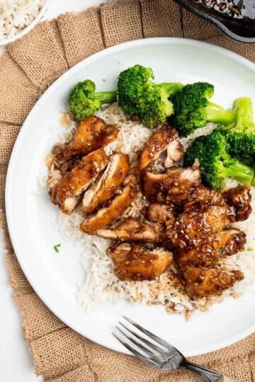 sliced honey garlic chicken over rice with broccoli on a white plate.