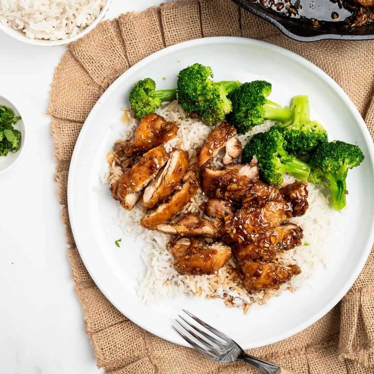 sliced honey garlic chicken over rice with broccoli on a white plate.