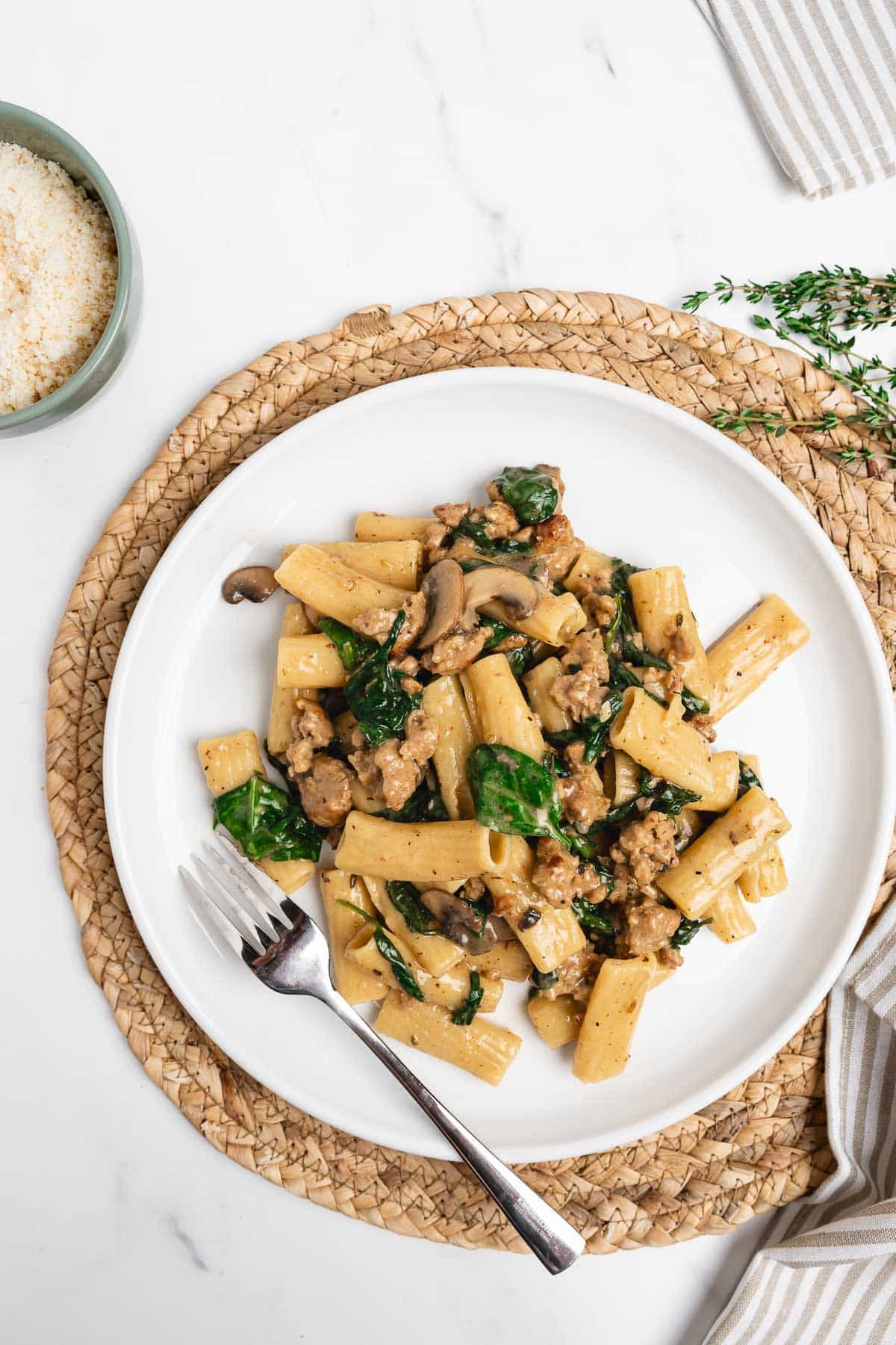 creamy Italian sausage pasta with spinach and mushroom on a white plate with a fork.