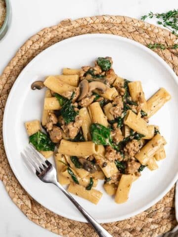 creamy Italian sausage pasta on a white plate with a fork.