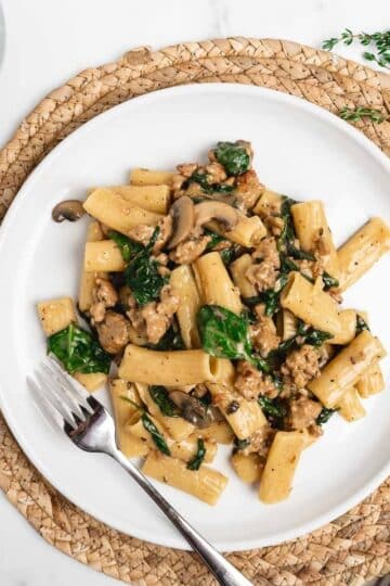 creamy Italian sausage pasta on a white plate with a fork.