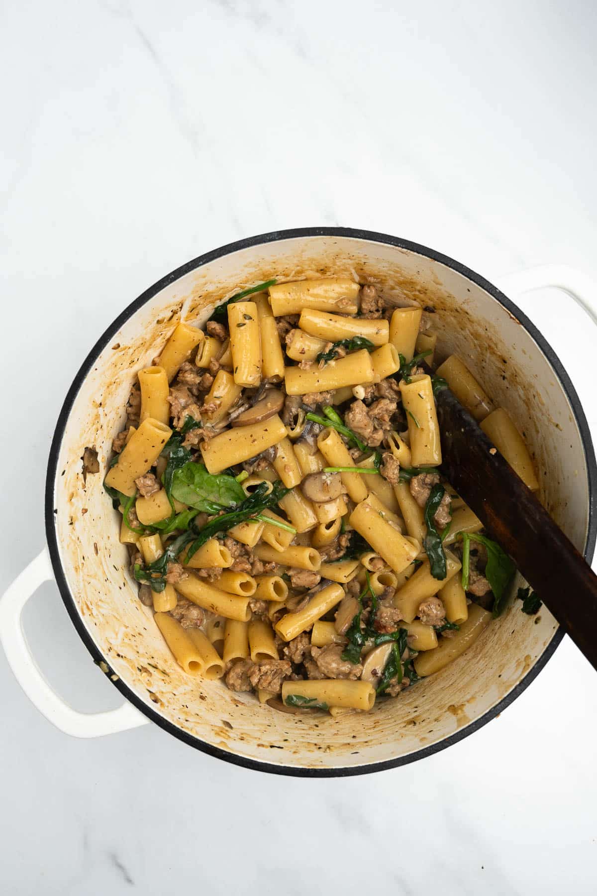 Italian sausage pasta in a pot with spinach and mushrooms.