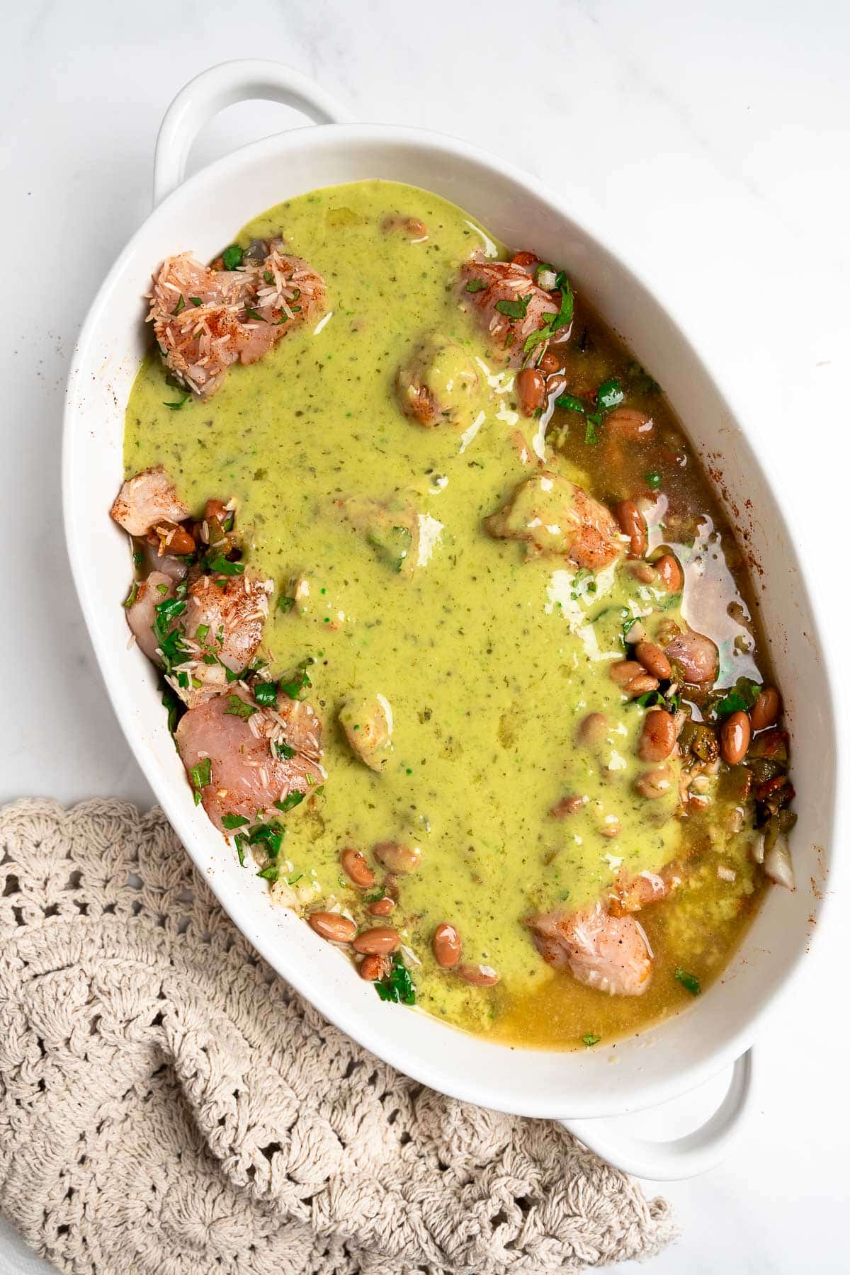 chicken, rice, cilantro, beans, spices with salsa verde and chicken broth in a baking dish.