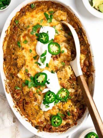 salsa verde chicken and rice in a baking dish topped with sour cream, jalapeños and cilantro.
